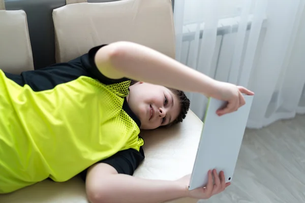 Chlapec hrát na tabletu vleže na gauči — Stock fotografie