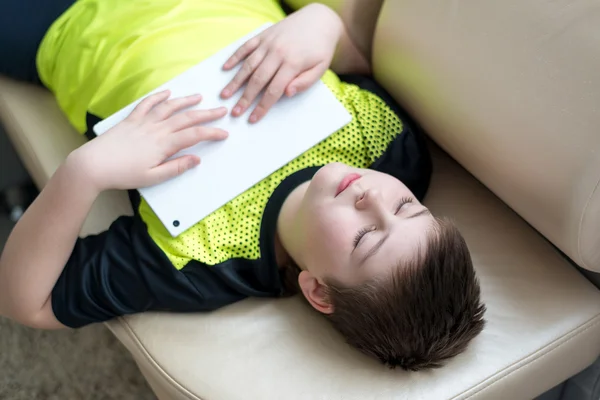 Pojke spelar på tavlan liggande på soffan — Stockfoto