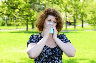 Woman closes nose with a tissue in park, pollinosis clipart