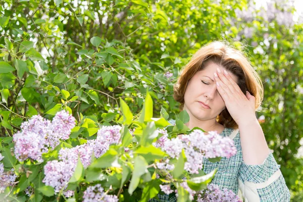 Žena trpící migrénou o kvetoucí šeřík — Stock fotografie
