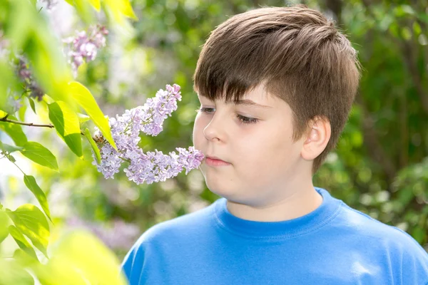 Chico oliendo una flor lila en el parque — Foto de Stock