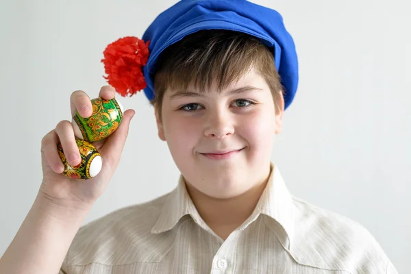 Menino em boné nacional russo com cravos segurando ovos de páscoa — Fotografia de Stock