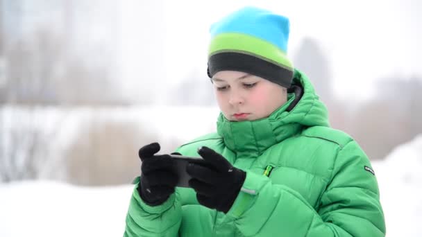 Jongen maakt gebruik van een mobiele telefoon met handschoenen buiten in de winter — Stockvideo