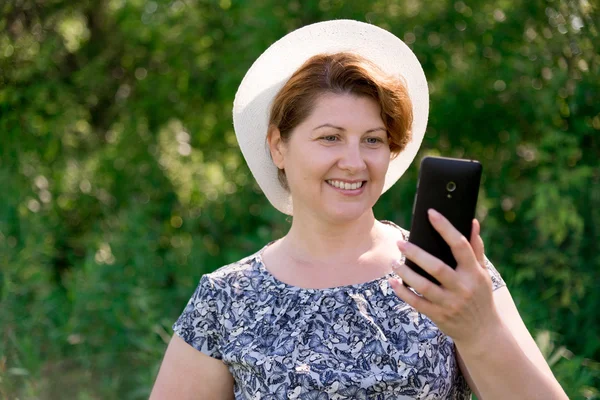 Woman in hat looks at cell phone outside — Stock Photo, Image