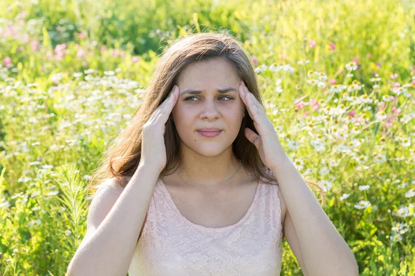 Menina adolescente com uma dor de cabeça em um prado florescente — Fotografia de Stock