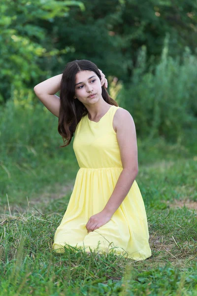 Das Mädchen im gelben Kleid sitzt auf dem Gras — Stockfoto