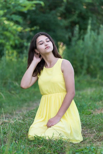 Het meisje in gele jurk zitten op gras — Stockfoto