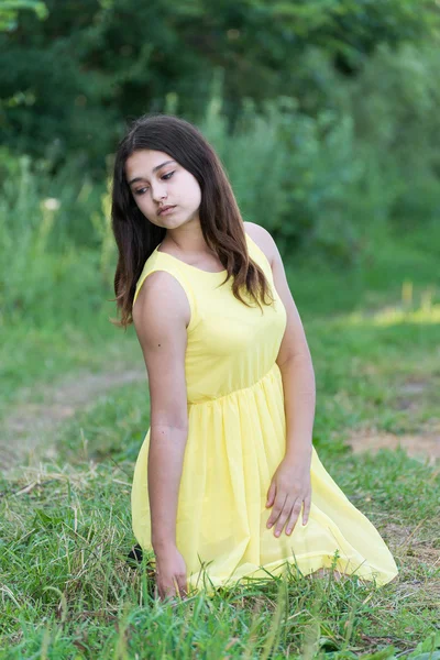 Menina em vestido amarelo sentado na grama ao ar livre . — Fotografia de Stock