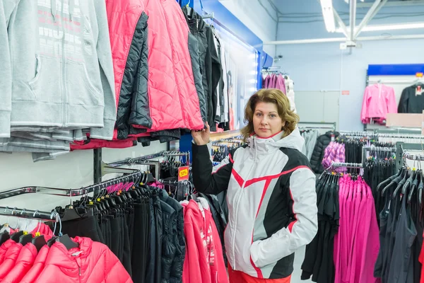 middle-aged woman chooses clothes in  sports shop