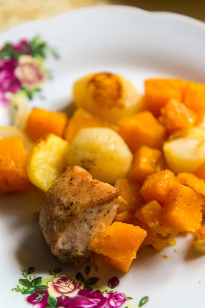 Курица, запечённая с ломтиками картошки и тыквой на тарелке — стоковое фото