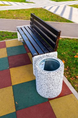 Çöp tenekesi ahşap bankın yanında.