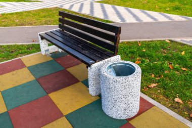 Çöp tenekesi ahşap bankın yanında.