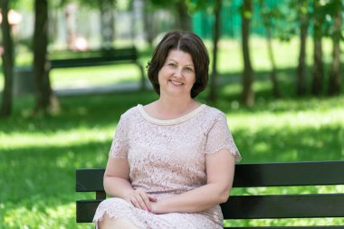 Dantel elbiseli kadın parkta bankta oturuyor.