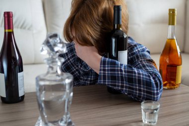 Şarap şişeleriyle masada oturan sarhoş kadın.