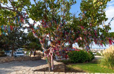 Protaras, Kıbrıs Cumhuriyeti - 10 Haziran. 2019. Hz. Elijah Kilisesi 'nin yanında renkli dilek kurdeleleri olan ağaç.