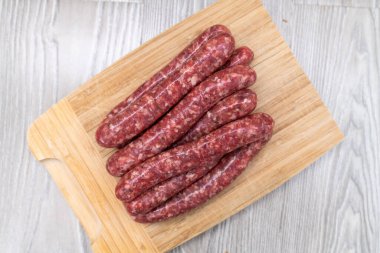 Ev yapımı çiğ sosisler tahta bir tahtanın üzerinde yatıyor.