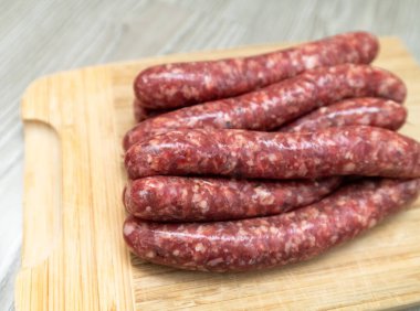 Ev yapımı çiğ sosisler tahta bir tahtanın üzerinde yatıyor.