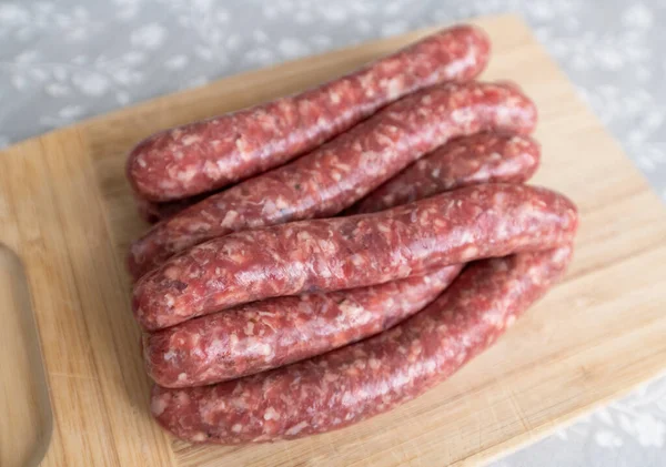 Homemade raw sausages lie on a wooden board — Stock Photo, Image