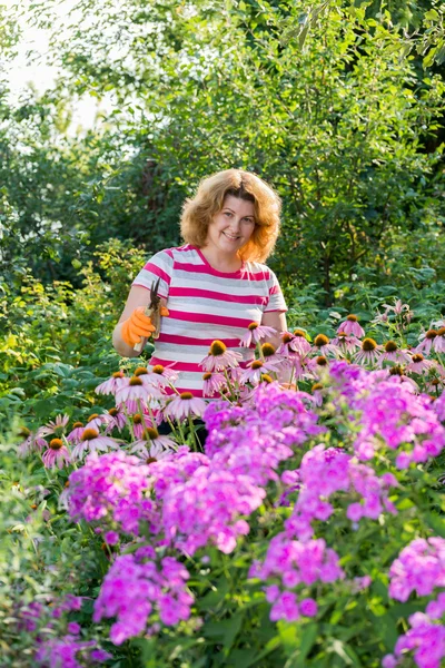 Pretty woman looks after behind plants in garden — Stock Photo, Image