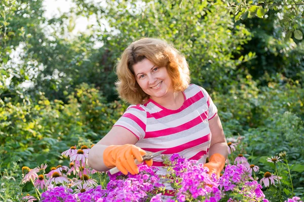 Pretty woman looks after behind plants in garden — Stock Photo, Image