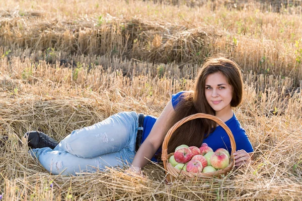 Teenie-Mädchen mit einem Korb voller Äpfel im Feld — Stockfoto