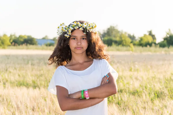 Tiener meisje met een krans van madeliefjes in veld — Stockfoto