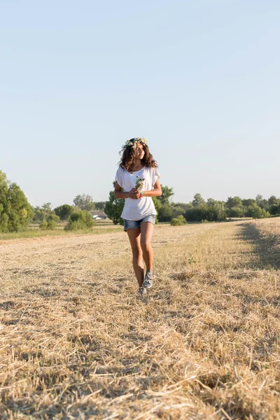 Tiener meisje in een krans van madeliefjes schreden in veld — Stockfoto