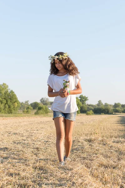 Adolescent fille dans une couronne de marguerites marche dans champ — Photo