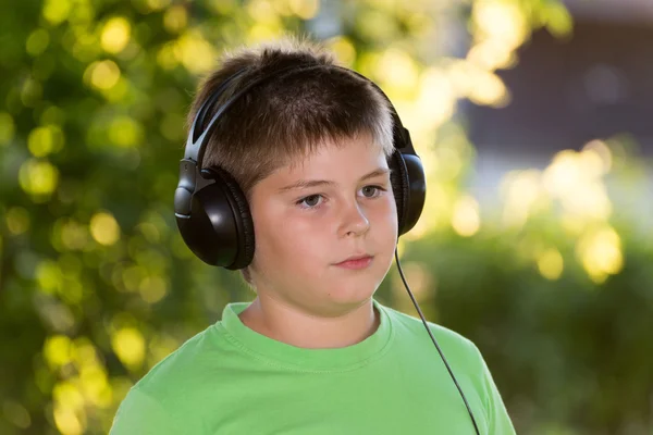 Niño escuchando música con auriculares en el parque — Foto de Stock