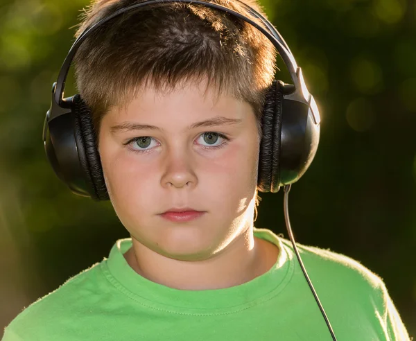 Menino ouvindo música com fones de ouvido no parque — Fotografia de Stock