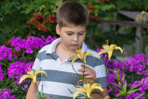 Menino adolescente sobre flores no jardim — Fotografia de Stock