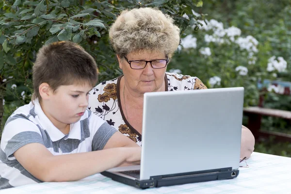 Farmor med en sonson bakom den laptop utomhus — Stockfoto