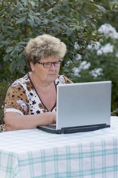 Ältere Frau arbeitet im Garten am Computer — Stockfoto