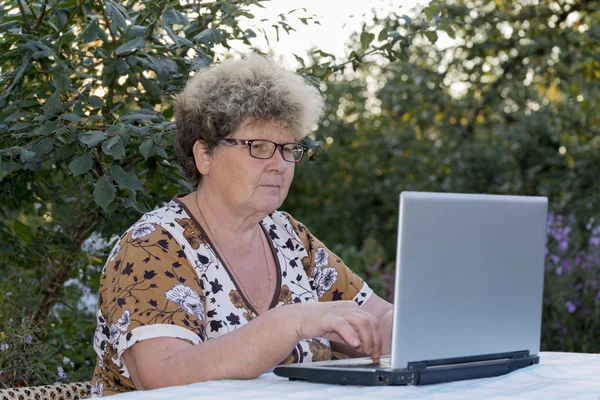 Bahçedeki bilgisayarda çalışan yaşlı kadın — Stok fotoğraf