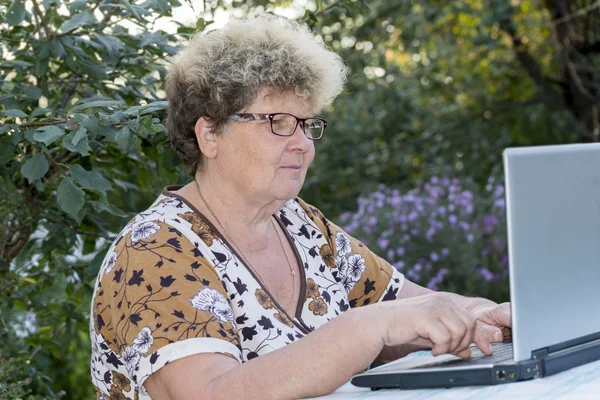 Пожилая женщина работает за компьютером в саду — стоковое фото