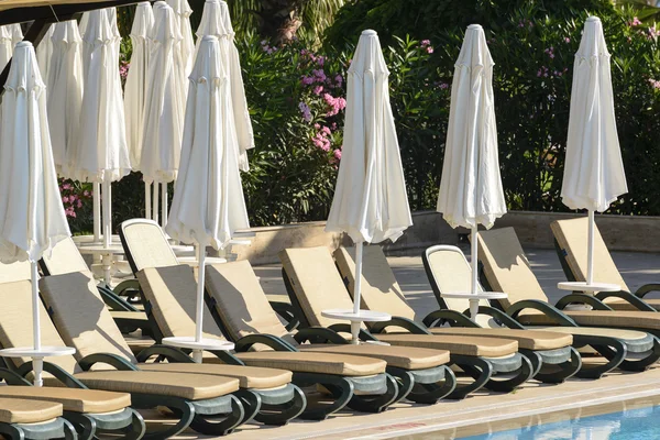 Espreguiçadeiras e guarda-sóis por piscina — Fotografia de Stock