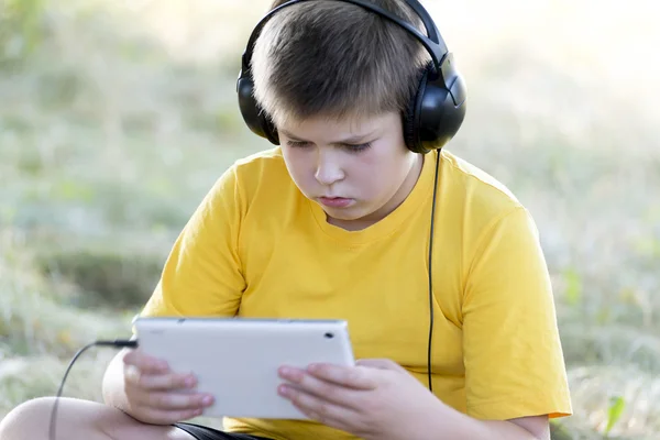 Jongen in hoofdtelefoons op zoek tablet pc over de aard — Stockfoto