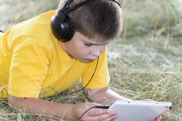 Garçon dans les écouteurs regarder tablette ordinateur sur la nature — Photo