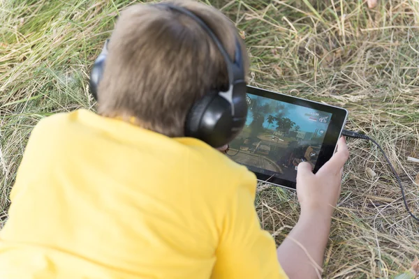 Garçon dans les écouteurs regarder tablette ordinateur sur la nature — Photo