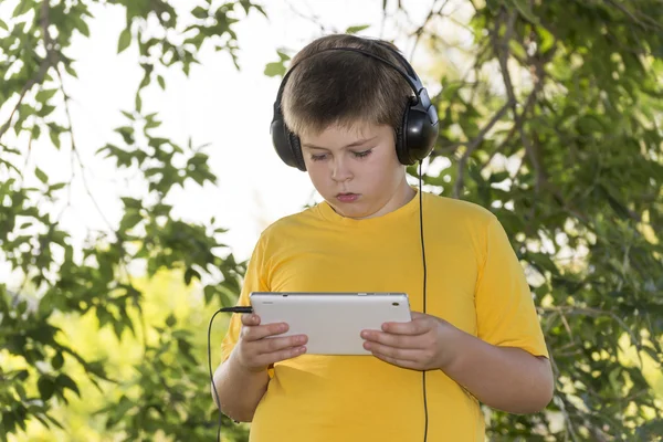 Pojken i hörlurar letar du tablet PC på natur — Stockfoto