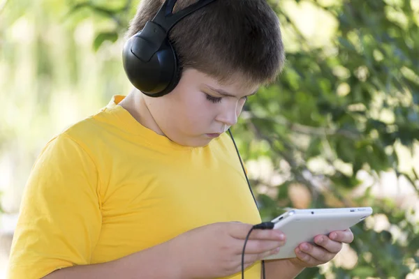Мальчик в наушниках смотрит планшетный компьютер на природу — стоковое фото