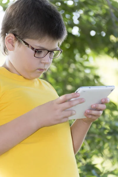 The boy in glasses looks tablet computer at nature — Stock Photo, Image