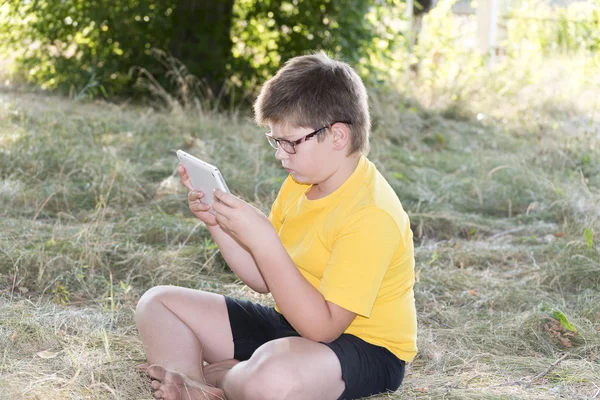 The boy in glasses looks tablet computer at nature — Stock Photo, Image