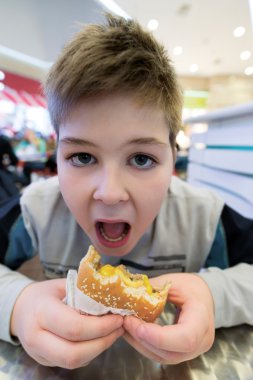 Genç çocuk hamburger n Cafe yiyor