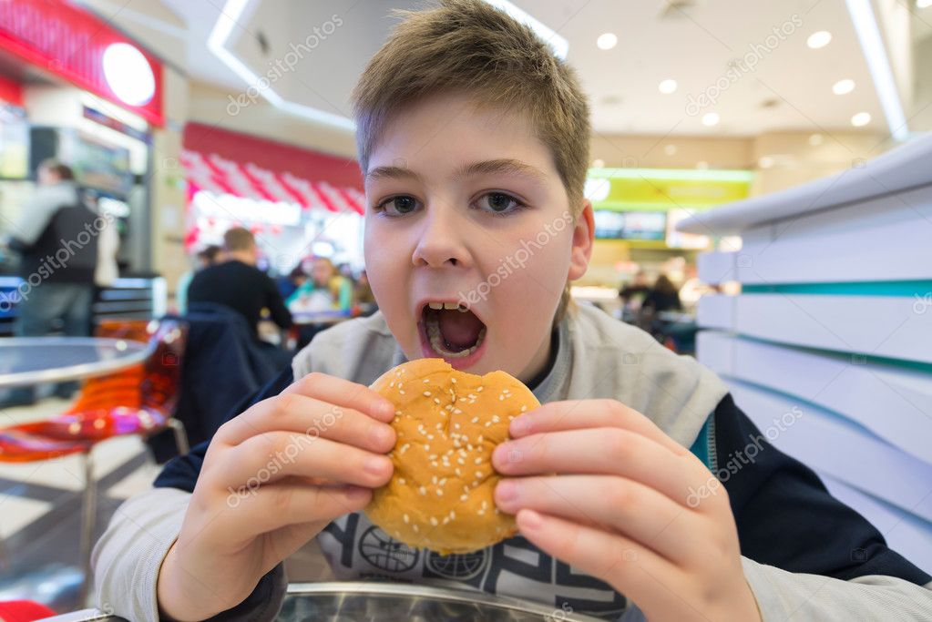 Teen boy eats hamburger n Cafe Stock Photo by ©olenka2008 59030379