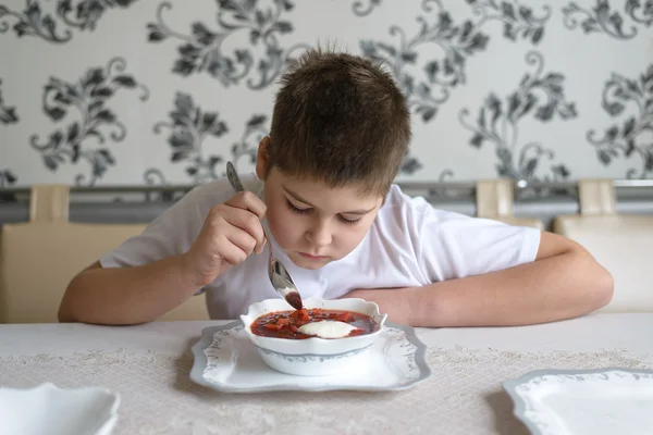 Menino adolescente comendo sopa na mesa da cozinha — Fotografia de Stock