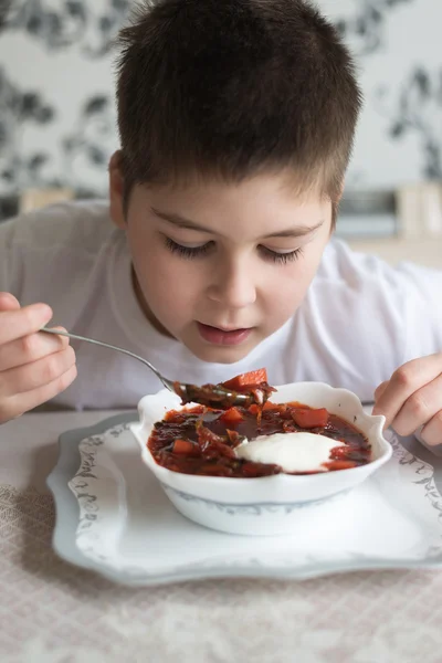Menino adolescente comendo sopa na mesa da cozinha — Fotografia de Stock