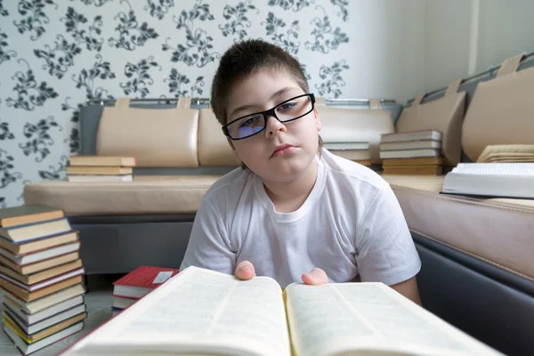 Silmälasipäinen poika lukemassa kirjaa huoneessa — kuvapankkivalokuva