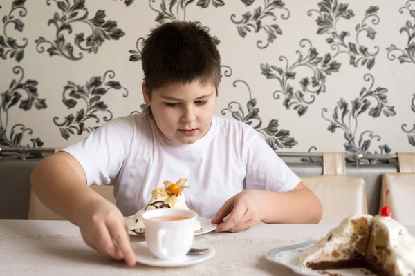 Çocuk çay pasta ile masada içiyor.