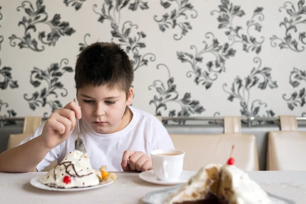 Мальчик пьет чай с тортом за столом — стоковое фото